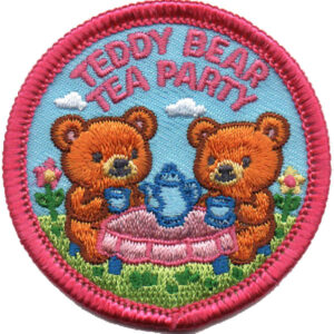 A colorful embroidered patch with two teddy bears having tea at a table. Pink text above reads “Teddy Bear Tea Party.” The background features flowers, grass, and clouds, with a pink border around the patch.