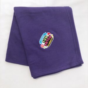 A folded Carolina blue blanket featuring a colorful "Patch Blanket" logo patch with flowers and playful text sewn at the center, displayed on a plain white background.