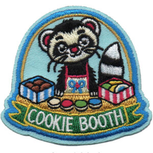 The Cookie Booth Patch is an embroidered patch showing a smiling cartoon raccoon in a red apron behind a table with cookies and boxes, above the words "COOKIE BOOTH" in green and white.