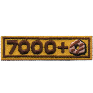 A rectangular embroidered patch called "1000+ Patch (Copy)" features a yellow background, brown border, and brown "7000+" text with a small donut next to the plus sign.