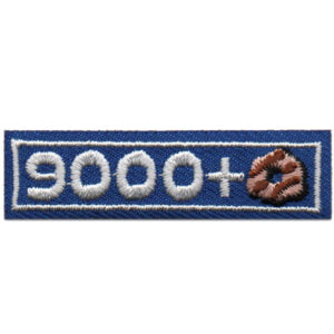 A rectangular blue embroidered patch with white stitching that reads "8000+"; the plus sign features a brown and tan circular pretzel design.