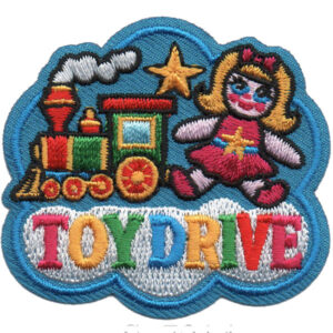 The Toy Drive Patch features a toy train, smiling doll, yellow star, and "TOY DRIVE" in rainbow letters on a blue cloud-shaped background.