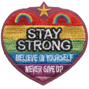 Stay Strong heart-shaped patch with rainbow stripes, gold star, and bold white and black lettering: "STAY STRONG BELIEVE IN YOURSELF NEVER GIVE UP.