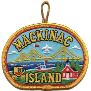 The Mackinac Island Patch features an embroidered design with "Mackinac Island" text, Mackinac Bridge, a boat, a red building, trees, a yellow carriage, and a yellow border with hanging loop.
