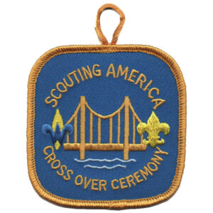 The Cross Over Ceremony BSA Patch (Copy) is a square patch with a gold border, featuring a bridge, two fleur-de-lis symbols, and "Scouting America Cross Over Ceremony" on blue, plus an orange hanging loop at the top.