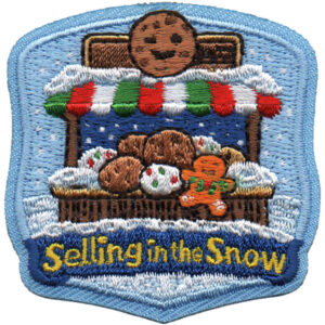 The Selling in the Snow Patch features an embroidered cookie stand with cookies, snow, an orange cookie character, and a red, white, and green striped awning. "Selling in the Snow" is written at the bottom.