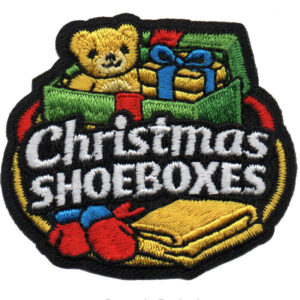 The Christmas Shoeboxes Patch features a colorful embroidered teddy bear, gift boxes, mittens, and a scarf above "Christmas Shoeboxes," with festive red, green, yellow, and blue accents.