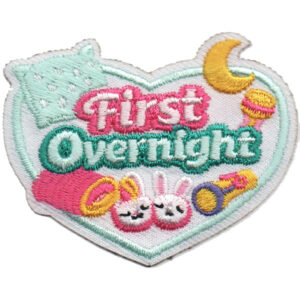 The First Overnight Patch is a heart-shaped embroidered patch featuring a pillow, moon, rattle, rings, slippers, and "First Overnight" in pink and green to celebrate a child's first overnight stay or sleepover.