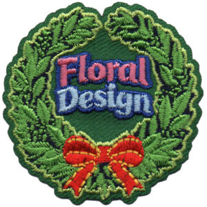 The Floral Design Patch (Copy) is a circular embroidered patch featuring a green leafy border, a red and yellow bow at the bottom, and "Floral Design" in pink and blue text at the center.