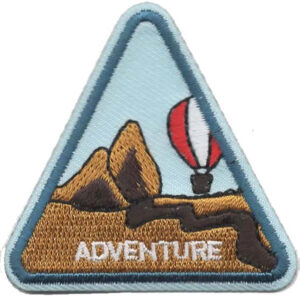 The Adventure Patch is a triangular badge featuring brown mountains, a red and white hot air balloon, and "ADVENTURE" embroidered at the bottom on a light blue background.